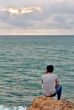 A man looks into the sea while sitting on a rock 