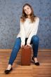 Beautiful young girl sitting on an old brown suitcase in the int