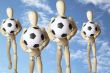 Four wooden figures with soccer balls in the sky