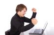 Business man raises arms in front of his laptop