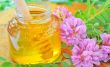 glass jar full of honey and stick with acacia pink and white flo