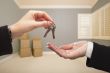 Realtor Handing Over the House Keys Inside Empty Grey Room