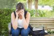 Upset Young Woman Sitting Alone on Bench Next to Books