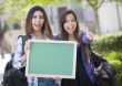 Mixed Race Female Students with Thumbs Up Holding Blank Chalkboa
