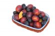 Vase in a wicker basket full of ripe plums and prunes.