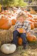 Little Boy Sitting and Holding His Pumpkin at Pumpkin Patch