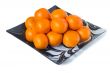 Large ripe tangerines in a glass dish on a white background.