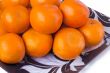 Large ripe tangerines in a glass dish on a white background.