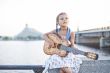 Girl playing guitar on river embankment