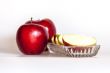 Two ripe red apples and segments of apple on a plate